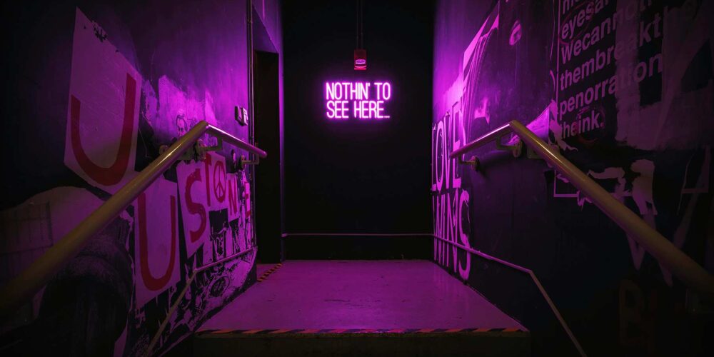 The image depicts a dark, narrow hallway with violet neon lights lining the walls. At the end of the hallway a door stands out, marked with the phrase 'Nothin' to see here…'.